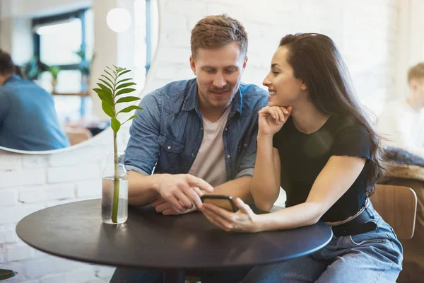 Lindo casal bela mulher e bonito homem verificando notícias no smartphone e beber café quente no café, olhando feliz — Fotografia de Stock