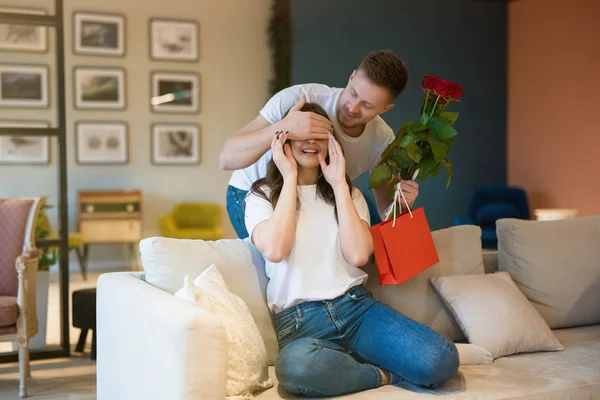 Ung man stänger sin frus ögon förbereder sig för att presentera sina röda rosor och gåva på helgonet alla hjärtans dag, glad årsdag — Stockfoto