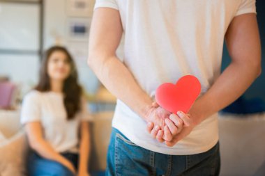 Güzel karısı için arkasında kırmızı kağıt kalp taşıyan genç bir adam. Mutlu romantik yıldönümleri, Sevgililer Günü.