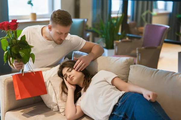 Ung vacker make överraskar sin vackra sovande älskade fru med rosor och gåva på helgonets alla hjärtans dag, glad romantisk årsdag — Stockfoto