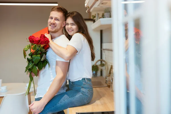 Jovem homem bonito surpreendendo sua amada esposa com rosas e presente no dia de São Valentim ambos olhando feliz sorrindo e abraçando, feliz aniversário romântico — Fotografia de Stock