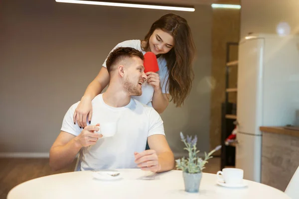 Ung vacker kvinna överraska sin man med papper hjärta på helgonet alla hjärtans dag under morgonen kaffe i köket, glad romantisk årsdag — Stockfoto