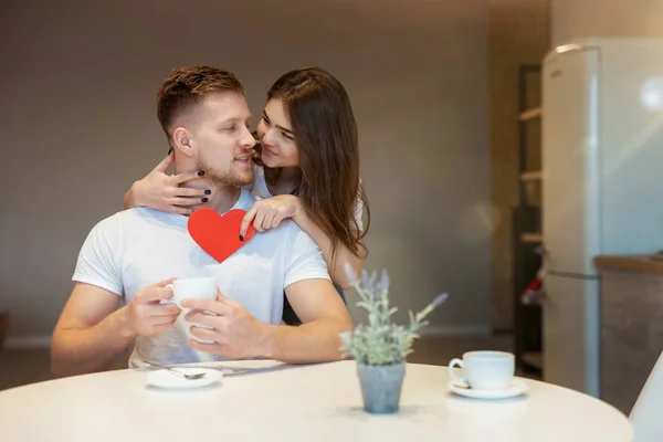 Ung vacker kvinna kramas och överraska sin man med rött papper hjärta på helgonet alla hjärtans dag under frukost i köket, glad romantisk årsdag — Stockfoto