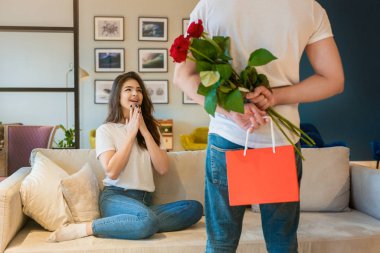 Kırmızı güller saklayan genç bir adam ve güzel sürpriz karısını karşılamak için arkasında bir hediye, mutlu romantik yıldönümü, Sevgililer Günü