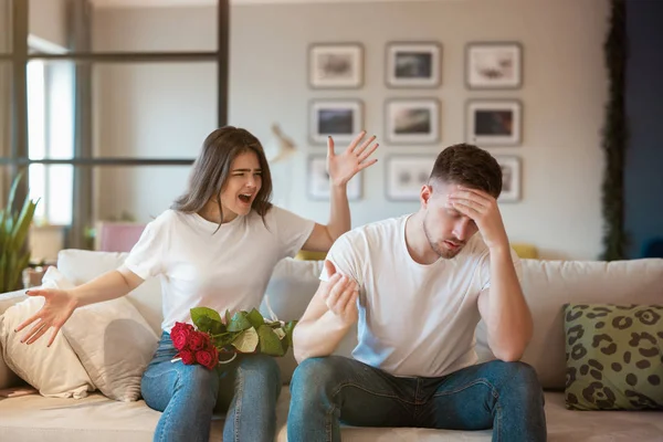 Young couple angry woman and tired handsome man both sitting on the sofa quarrelling on saint valentine's day, family drama — Stock Photo, Image