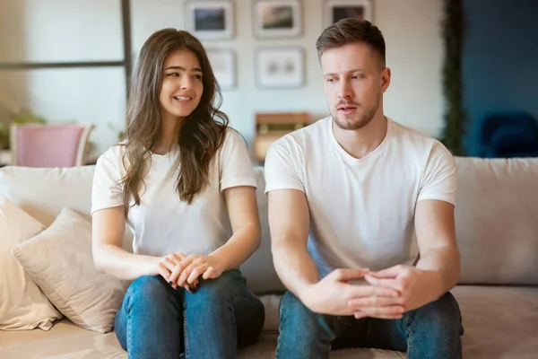 Jong stel man en vrouw zitten op de bank zowel kijken beschaamd, grimmige stemming — Stockfoto