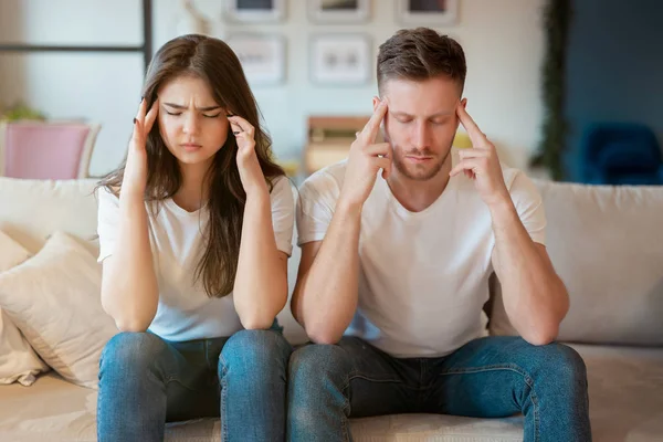 Jeune couple homme et femme assis sur le canapé à la fois l'air fatigué et épuisé, humeur grimaçante — Photo