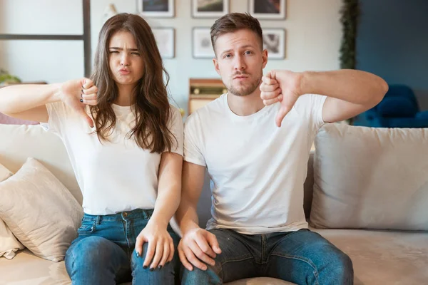 Unge parmenn og kvinner som sitter på sofaen og ser glade ut, begge viser et mislikt tegn, grimasende humør – stockfoto