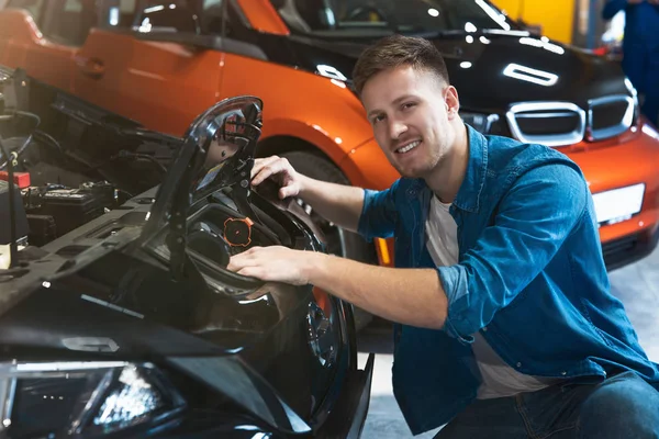 Cliente joven sentado cerca del capó abierto del vehículo que explora el motor eléctrico en el centro del concesionario del coche, concepto cero de la emisión — Foto de Stock