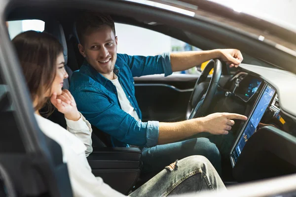 Joven pareja guapo hombre y hermosa mujer comprobar nuevo vehículo interior en coche eléctrico centro de concesionarios, momentos felices — Foto de Stock