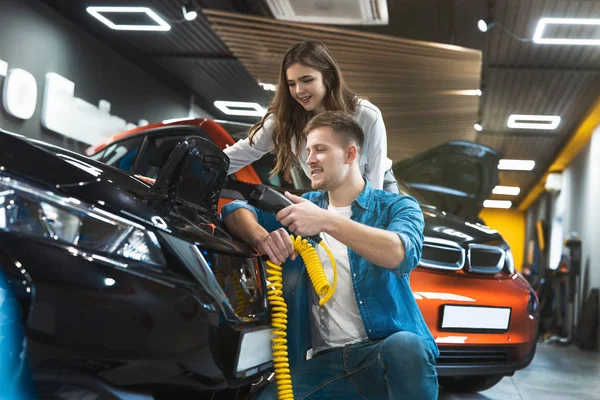 Joven familia pareja guapo hombre muestra su hermosa morena esposa cómo utilizar cable de carga para coche eléctrico, buscando feliz y emocionado — Foto de Stock