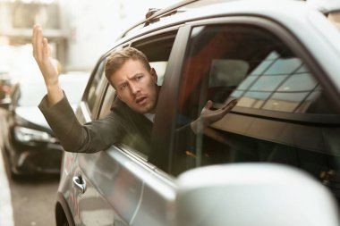 Genç işadamı, trafik sıkışıklığında açık arabanın camından dışarı bakarken gergin hissediyor.