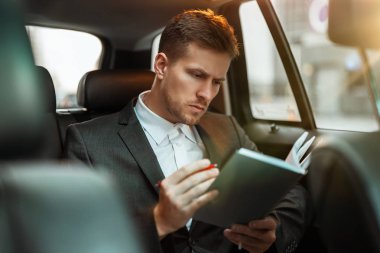 Genç ve başarılı iş adamı, ortaklarıyla buluşmaya giderken arabasında otururken planlayıcısına notlar alır.