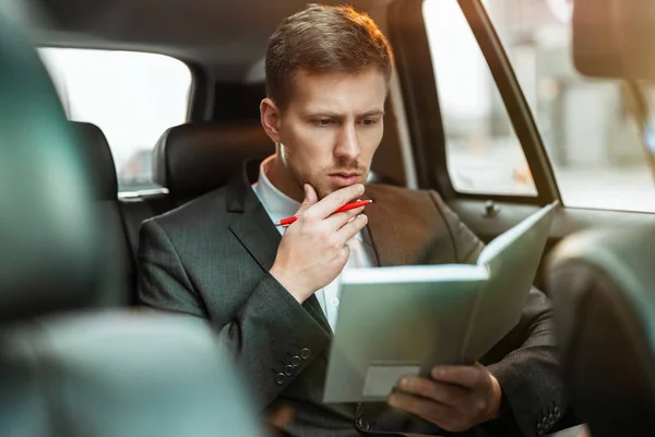 Успешный бизнесмен делает заметки своему планировщику во время езды на заднем сиденье автомобиля на пути к встрече с партнерами, выглядит вдумчивым, многозадачным концептом — стоковое фото