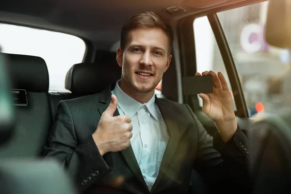 Sukces biznesmen dokonywania płatności online za pomocą karty bankowej podczas jazdy na tylnym siedzeniu samochodu pokazując jak znak, wygląda zadowolony, wielozadaniowość koncepcja — Zdjęcie stockowe