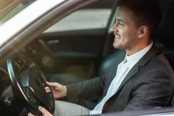 Bell'uomo d'affari sorridente e di successo sembra felice mentre guida la sua auto con finestra aperta, multitasking, grande vita di città — Foto Stock
