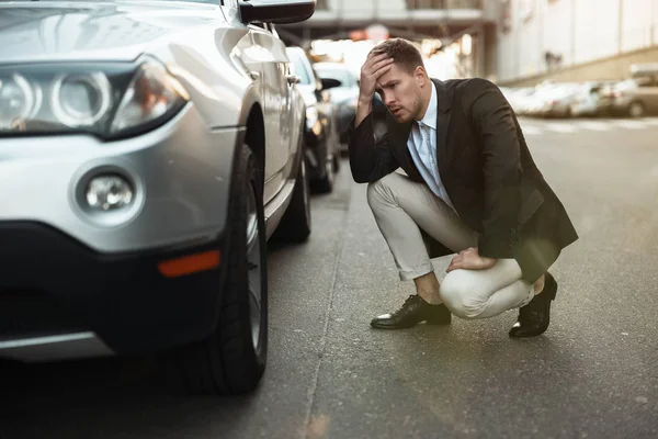 Junger gutaussehender Geschäftsmann, der das Lenkrad seines Autos überprüft, das auf der Straße Probleme hat, unerwartete Fahrzeugprobleme — Stockfoto