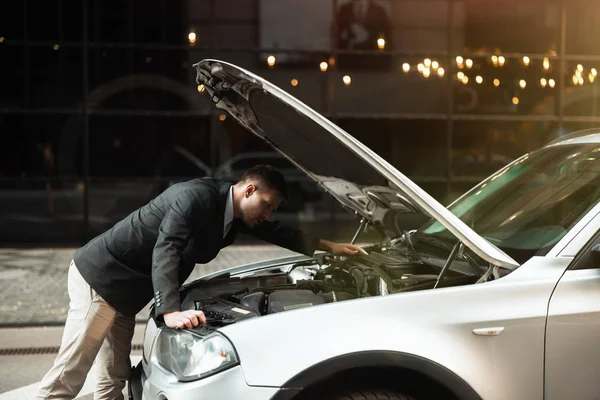 Joven hombre de negocios guapo de pie cerca de parachoques de coche delantero abierto, motor de comprobación, problemas inesperados del vehículo — Foto de Stock