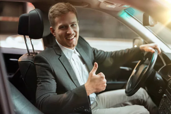 Joven hombre de negocios guapo conducir coche de lujo buscando satisfecho, mostrando como signo, concepto de estrategia exitosa — Foto de Stock