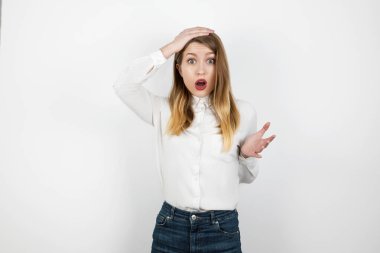 Genç, güzel, sarışın, kaybolmuş görünüyor. İzole beyaz arka planda duruyor. Kafasına dokunuyor, vücut dili kavramına.