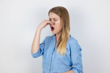Genç sarışın kadın burnunu kötü kokudan kapatıyor izole edilmiş beyaz arka planda duruyor, vücut dili...