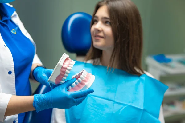 Tandläkare bär medicinska handskar visar unga beautifyul kvinna patient käken modell innan behandling i tandvårdskliniken, sjukvård koncept — Stockfoto