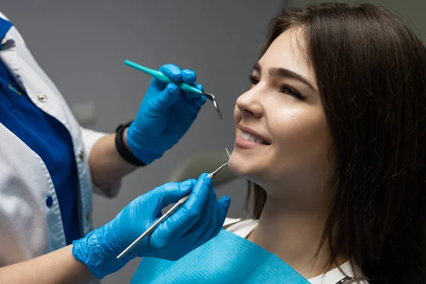 Lekarz dentysta w niebieskich rękawiczkach bada pacjentkę za pomocą lusterka stomatologicznego i skalera, gdy siedzi na krześle dentystycznym w klinice, koncepcja opieki zdrowotnej — Zdjęcie stockowe