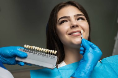 Diş emaye ölçeği mutlu kadın hasta dişleri için diş beyazlatma prosedürü için sağ gölge almak için örnek uygulayarak mavi tıbbi eldivenler diş hekimi