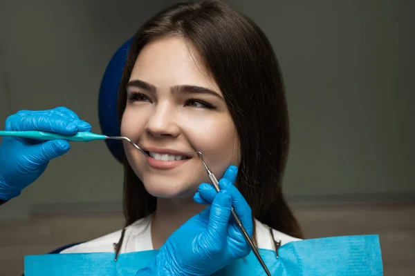 Morena paciente examinada por dentista en guantes azules usando espejo dental y escalador sentado medio turno en silla dental durante la cita, concepto de atención médica — Foto de Stock