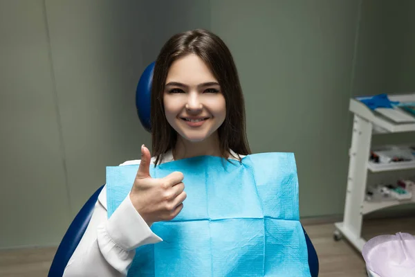 Krásná mladá usměvavá brunetka pacient žena s vyšetřením na zubní ordinaci ukazující jako znamení, vypadající šťastný, zdravotní koncepce — Stock fotografie