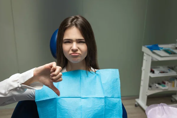 Krásná mladá rozrušená brunetka pacient žena s vyšetřením na zubní ordinaci ukazující nechutné znamení, vypadající nešťastně, zdravotní koncepce — Stock fotografie