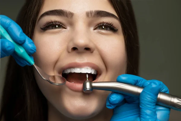 Dentysta w niebieskich rękawiczkach wypełniający piękny kanał korzeniowy uśmiechniętej kobiety pod lampą medyczną w klinice z bliska, koncepcja opieki zdrowotnej — Zdjęcie stockowe