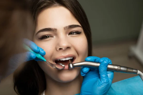Tandläkare i blå handskar fyller den vackra leende kvinnans patientens rotfyllning med spegel under den medicinska lampan på kliniken närbild, sjukvård koncept — Stockfoto