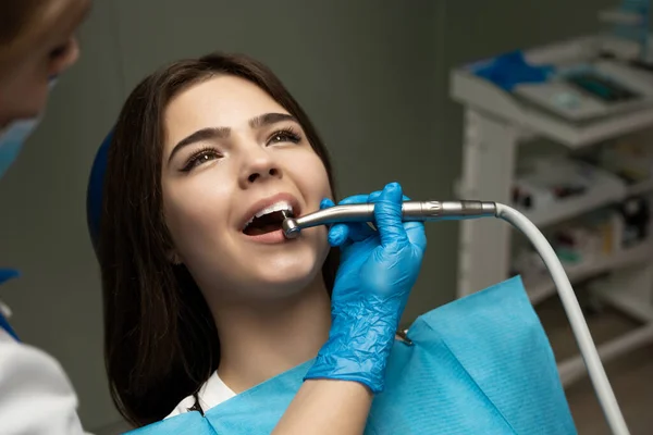 Brunett kvinna patient botas av tandläkare i blå handskar med hjälp av tandspegel och scaler sitter i tandstol under tandvård behandling på kliniken, helvård koncept — Stockfoto