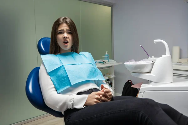 Krásná mladá vystrašená pacientka sedící v zubním křesle během vyšetření u zubního lékaře vypadá vystrašeně, zdravotní koncepce — Stock fotografie
