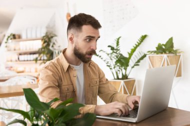 Genç ve yakışıklı bir adam öğle yemeği molasında laptopunda çalışıyor. Şaşırmış, çoklu görev kavramı, pozitif titreşimler..