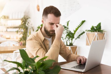 Genç ve yakışıklı bir adam öğle yemeği molasında laptopunda çalışıyor. Stresli görünüyor, birden fazla iş yapıyor, vücut dili kullanıyor..