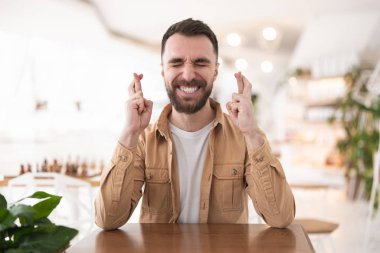 Genç yakışıklı sakallı adam şans dilemek için dua ediyor. Kafede otururken, vücut dili konsepti..