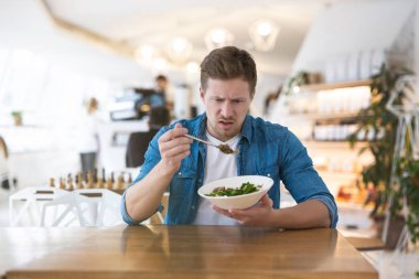 Genç yakışıklı adam öğle yemeğinde salatasından memnun değil gibi görünüyor. Şikayet ve öneri konsepti..
