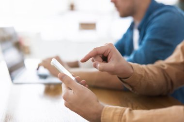 Bir adam dizüstü bilgisayarını ve bir diğeri de parmaklarıyla akıllı telefon, insan ve dijital teknoloji kavramını kullanıyor..