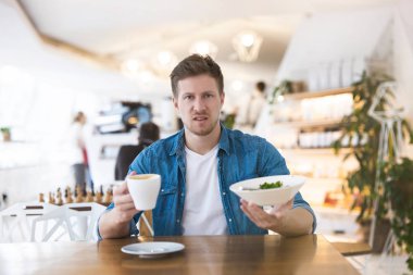 Genç yakışıklı adam, öğle yemeği sırasında kafeteryada yiyecek ve içeceklerin kalitesinden, şikâyetlerden ve önerilerden memnun değil gibi görünüyor..