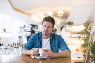 Genç ve yakışıklı bir adam kafeteryada öğle yemeği arasında kahve içiyor. Düşünceli ve düşünceli görünüyor..