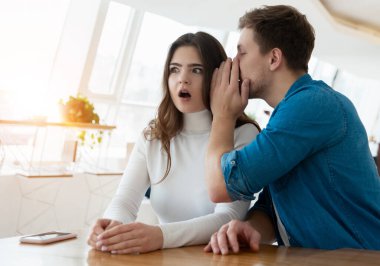 Kafede oturan genç çift, yakışıklı adam güzel bir kadının kulağına bir şeyler fısıldıyor, şaşırmış görünüyor, dedikodu konsepti..