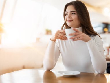 Genç ve güzel bir kadın öğle yemeği molasında kafede kahve içiyor, sakin görünüyor, huzur ve rahatlama kavramı..