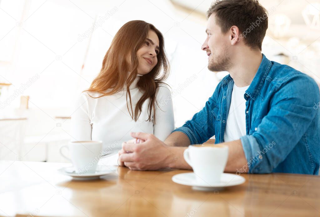 young couple beautiful woman holding hands with her handsome man while drinking coffee in cafe during lunch time break, love and tenderness concept.