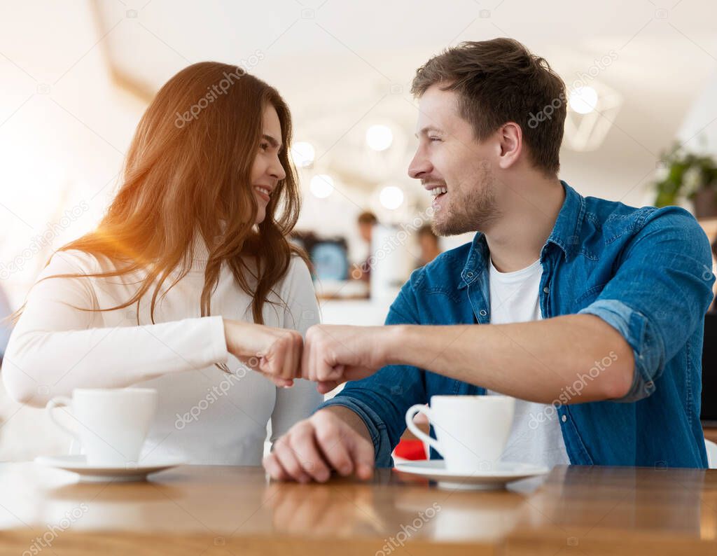 young happy brunette woman and handsome man clenching their fists in winning position after successful cooperation while drinking coffee in cafe, body language concept.