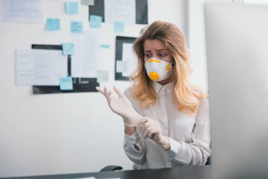 Korunma maskeli genç sarışın kadın yönetici, Covid-19 epidemisi ve virüs bilimi konsepti sırasında çalışırken tıbbi koruma eldiveni takmaktan korkmuş görünüyor..