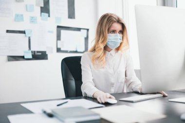 Tıbbi koruma maskesi ve eldiven giyen genç sarışın kadın yönetici Covid-19 epidemi, virüs bilimi konsepti sırasında ofiste çalışıyor..
