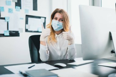 Tıbbi koruma maskesi ve eldiven giyen genç sarışın kadın yönetici Covid-19 epidemisi sırasında ofiste çalışıyor..