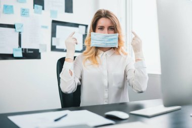 Tıbbi koruma eldivenleri takan genç sarışın kadın yönetici Covid-19 epidemi, virüs bilimi konsepti sırasında ofiste çalışırken maske takıyor..